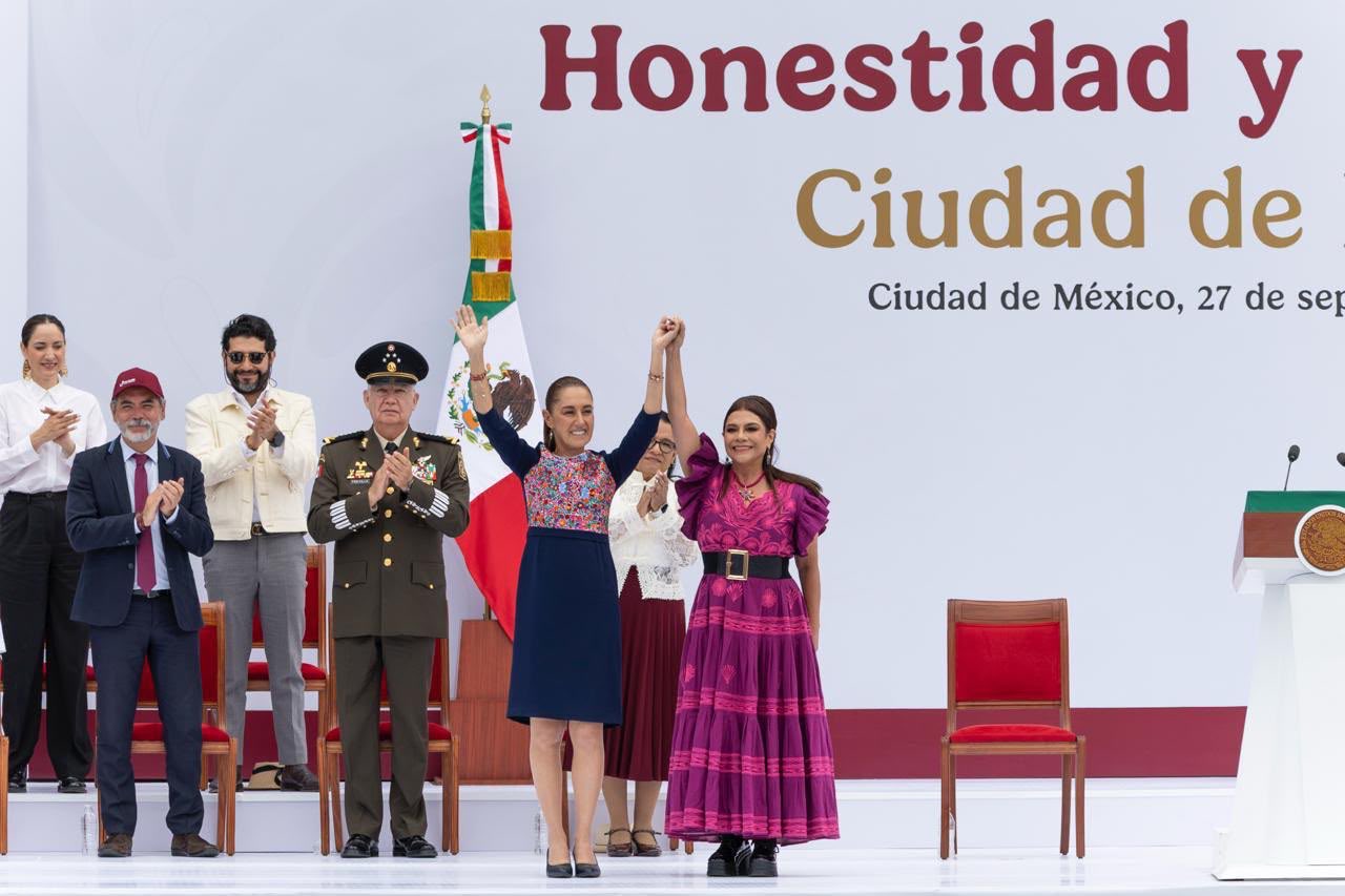 Claudia Sheinbaum y Clara Brugada levantan las manos unidas en el templete del Zócalo, acompañadas de autoridades.